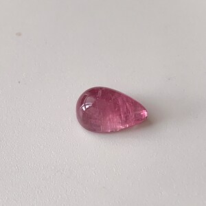K&ouml;nnte beinhalten: Ein tropfenf&ouml;rmiger rosa Edelstein mit einer glatten, polierten Oberfl&auml;che.