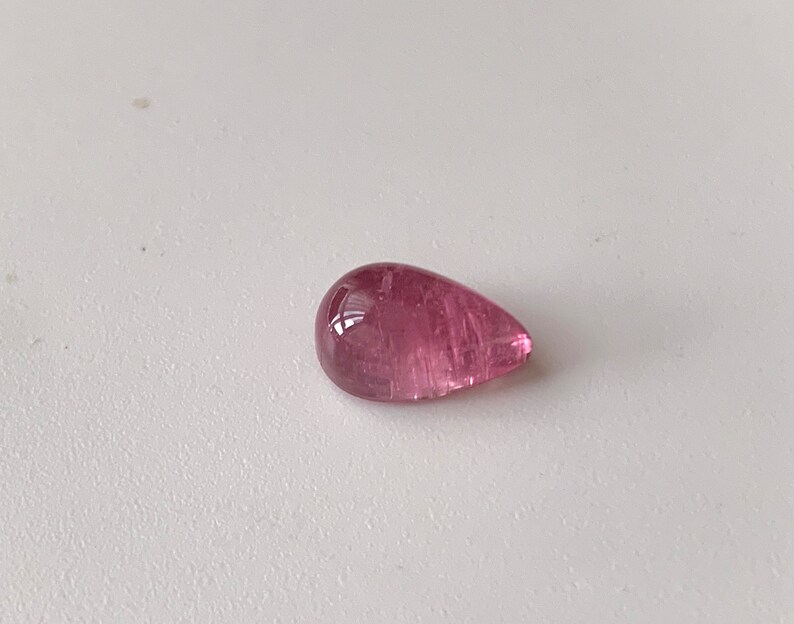K&ouml;nnte beinhalten: Ein tropfenf&ouml;rmiger rosa Edelstein mit einer glatten, polierten Oberfl&auml;che.