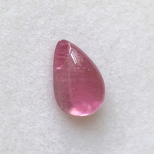 K&ouml;nnte beinhalten: Ein tropfenf&ouml;rmiger rosa Edelstein mit einer glatten, polierten Oberfl&auml;che.