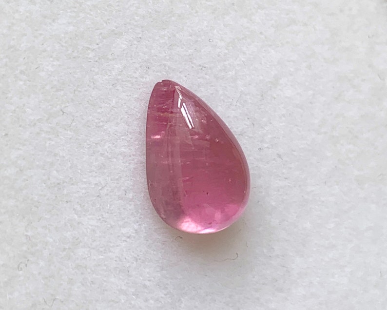 K&ouml;nnte beinhalten: Ein tropfenf&ouml;rmiger rosa Edelstein mit einer glatten, polierten Oberfl&auml;che.