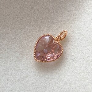 K&ouml;nnte beinhalten: Ein herzf&ouml;rmiger Anh&auml;nger aus Ros&eacute;gold mit einem rosa Kristall. Der Anh&auml;nger hat einen zarten Perlenrand.