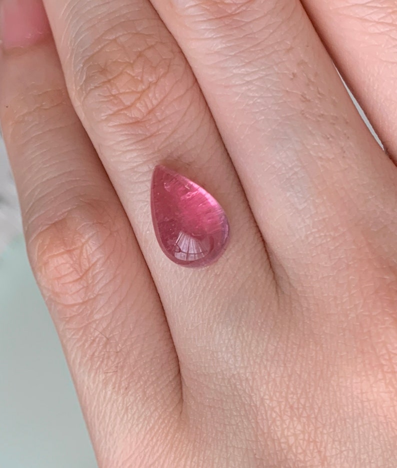 K&ouml;nnte beinhalten: Ein tropfenf&ouml;rmiger rosa Edelstein mit einer glatten, polierten Oberfl&auml;che.
