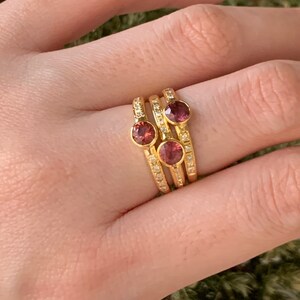 May include: Three gold rings with small pink gemstones and a row of tiny clear stones on each band.