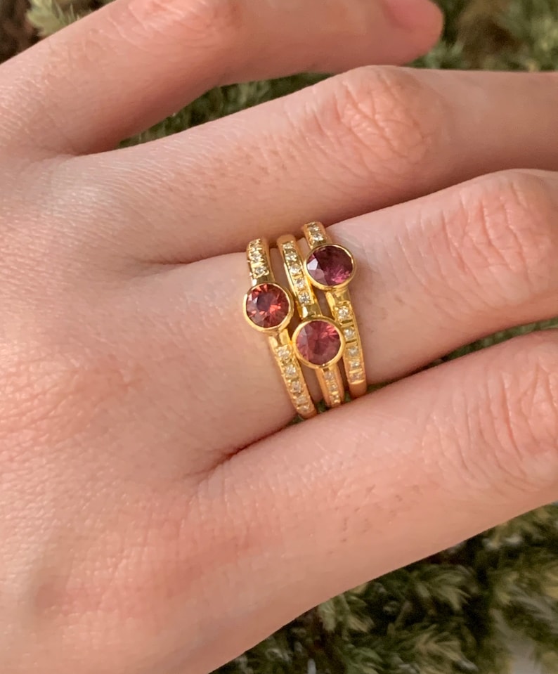 May include: Three gold rings with small pink gemstones and a row of tiny clear stones on each band.