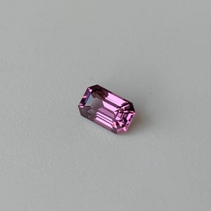 May include: A pink gemstone with a rectangular emerald cut.