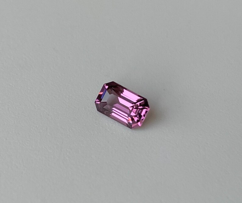 May include: A pink gemstone with a rectangular emerald cut.