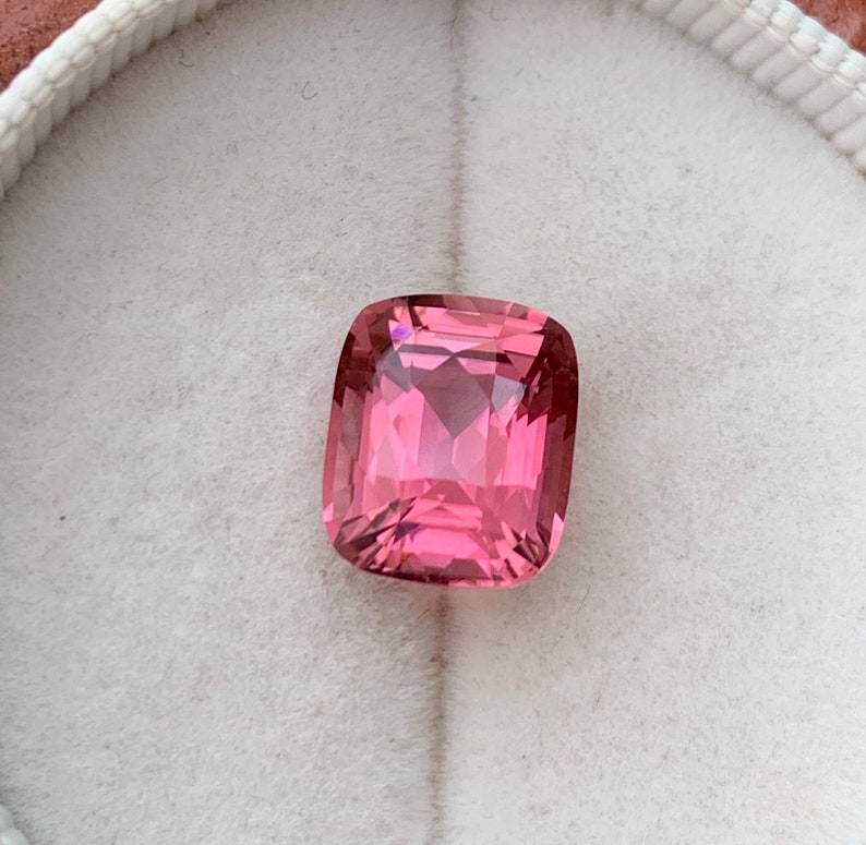 Puede incluir: Una piedra preciosa rosa de talla coj&iacute;n con forma cuadrada. La piedra preciosa est&aacute; colocada sobre un fondo blanco.