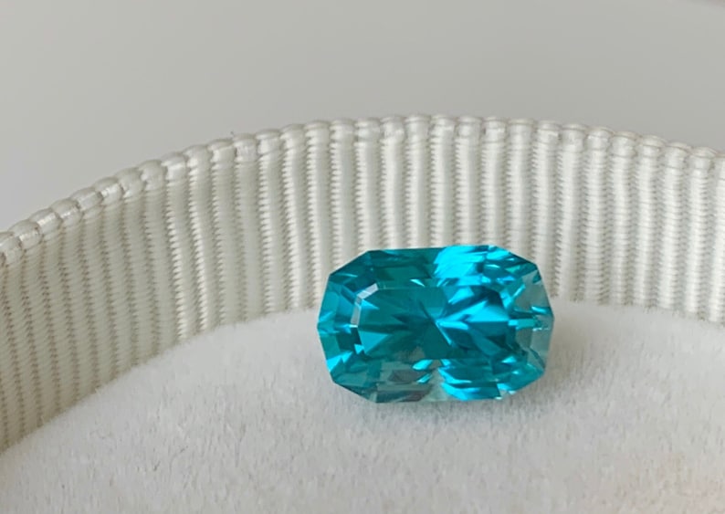 Puede incluir: Una gema azul vibrante con un corte rectangular, mostrada sobre un fondo blanco.
