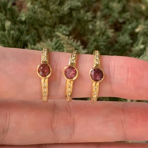 May include: Three gold rings with a single round pink gemstone and a band of small white gemstones.