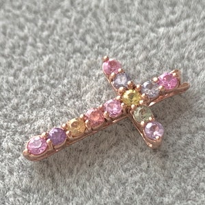 May include: A small gold cross pendant with colorful gemstones. The cross is adorned with pink, purple, yellow, and green gemstones.
