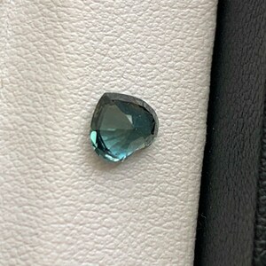 May include: A heart-shaped gemstone with a blue-green hue. The gemstone is set against a white background.