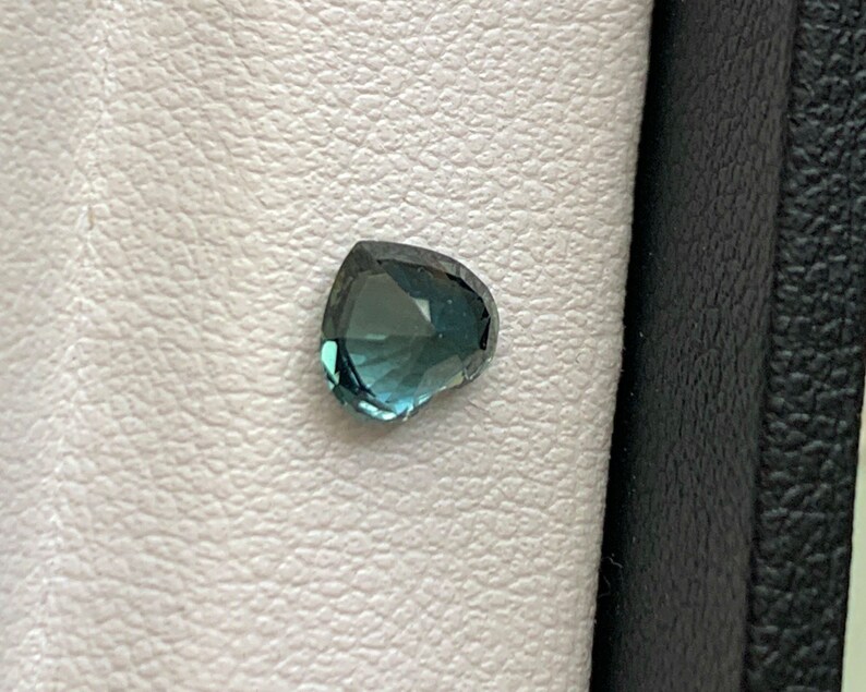 May include: A heart-shaped gemstone with a blue-green hue. The gemstone is set against a white background.