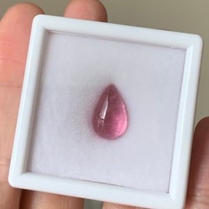 K&ouml;nnte beinhalten: Ein tropfenf&ouml;rmiger rosa Edelstein in einer wei&szlig;en Pr&auml;sentationsbox.