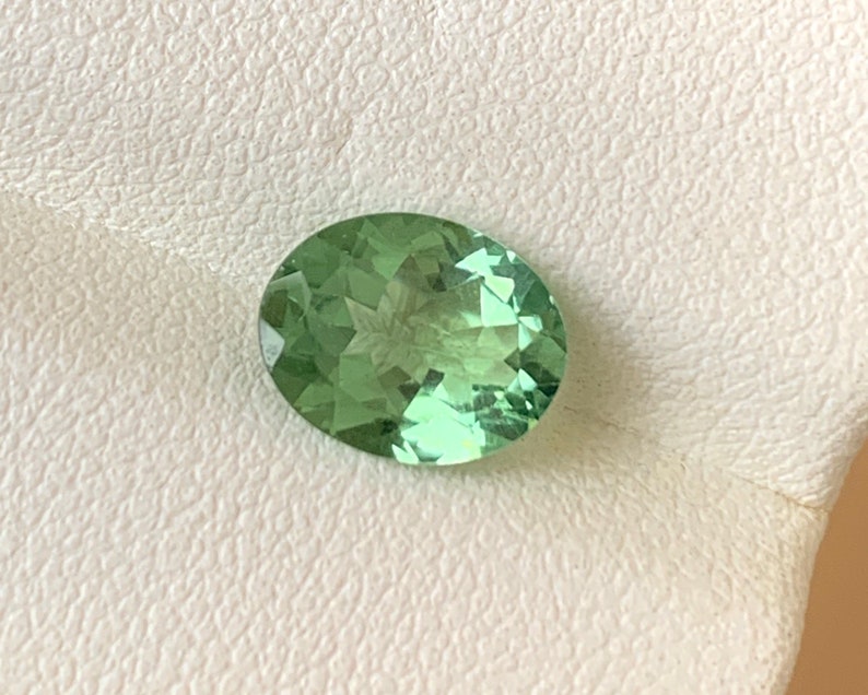 May include: A light green oval-shaped gemstone with a star-like pattern inside.