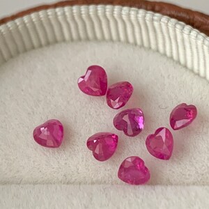 May include: A collection of eight pink heart-shaped gemstones in a white velvet-lined box.