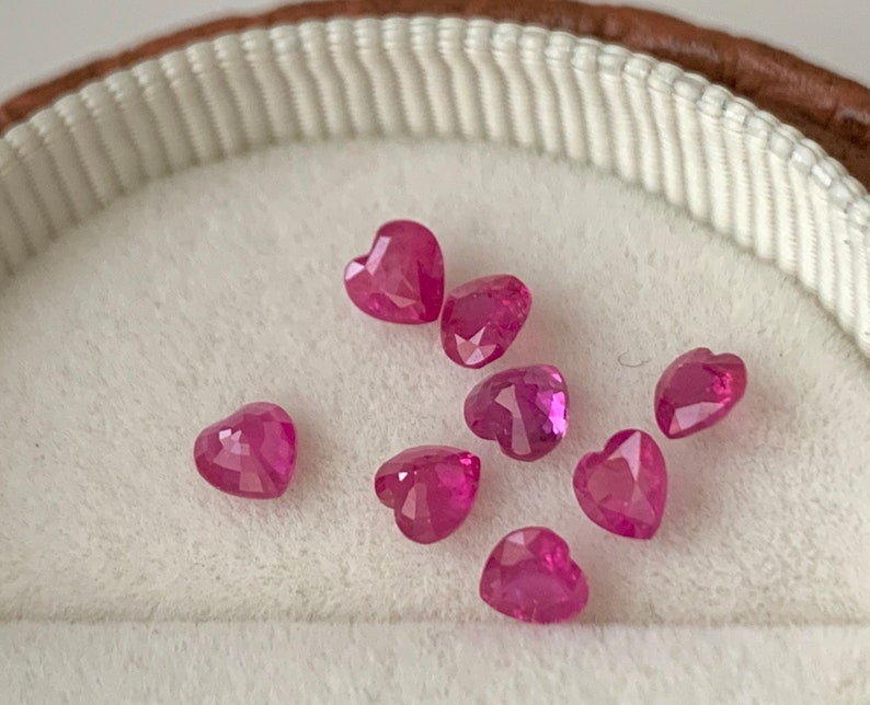 May include: A collection of eight pink heart-shaped gemstones in a white velvet-lined box.