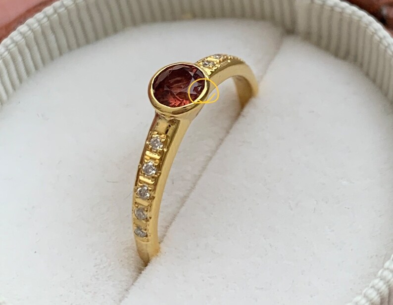May include: A gold ring with a single red gemstone and a row of small diamonds on the band.