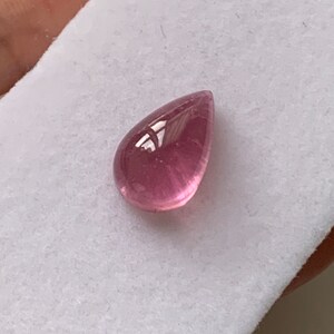 K&ouml;nnte beinhalten: Ein tropfenf&ouml;rmiger rosa Edelstein mit einer glatten, polierten Oberfl&auml;che.