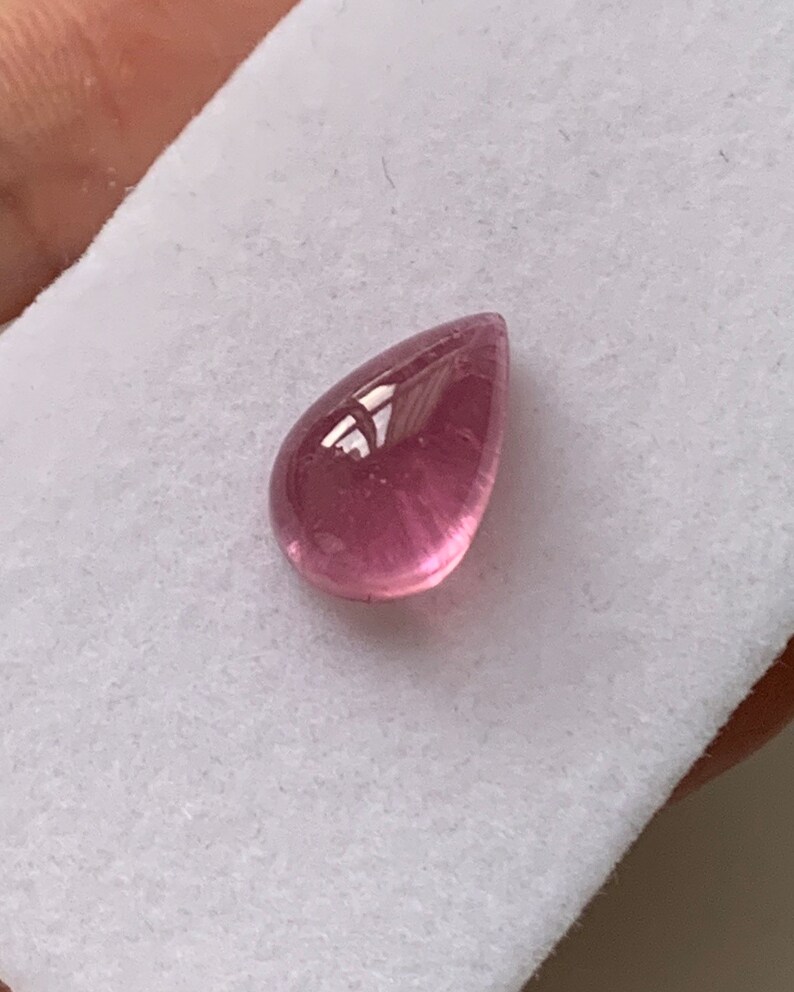 K&ouml;nnte beinhalten: Ein tropfenf&ouml;rmiger rosa Edelstein mit einer glatten, polierten Oberfl&auml;che.