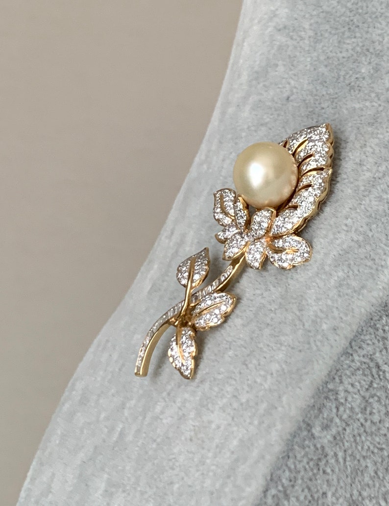May include: A gold-tone brooch featuring a pearl and clear rhinestones in a floral design.