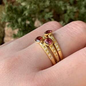 May include: Three gold rings with a row of small diamonds and a single pink gemstone on each ring.