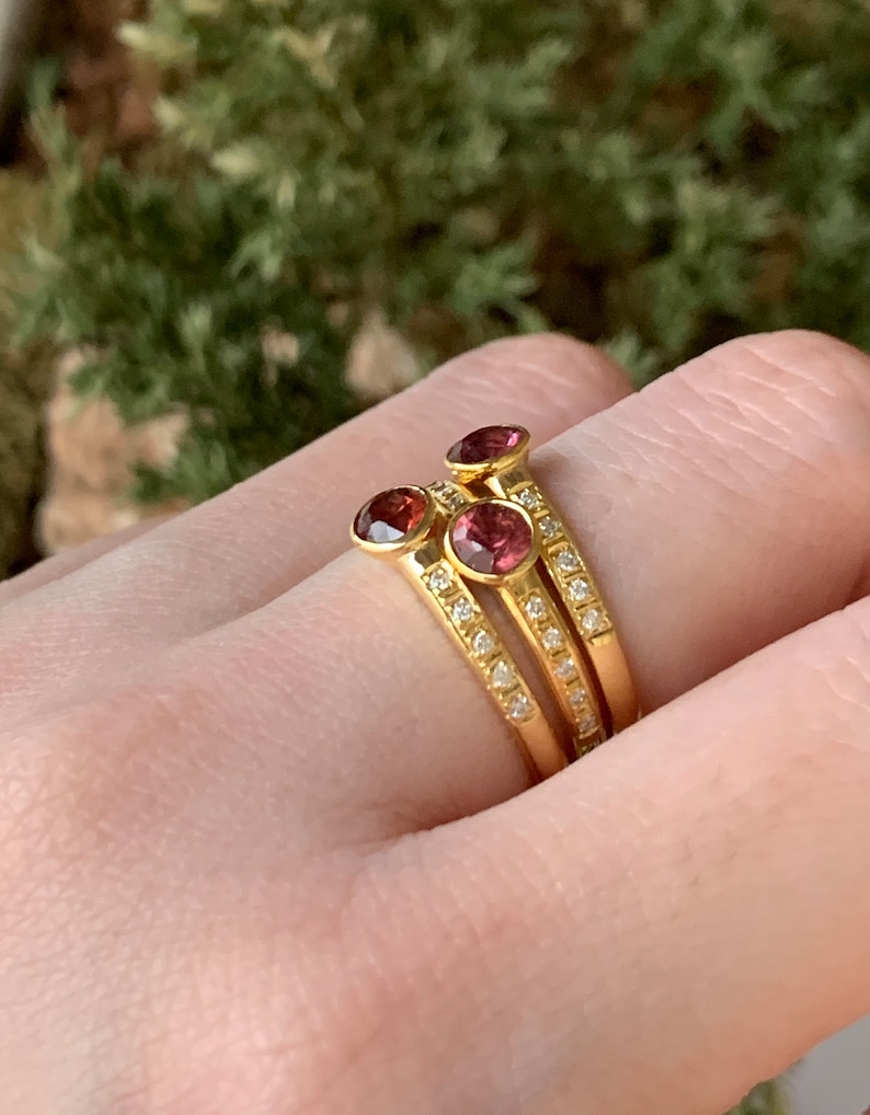 May include: Three gold rings with a row of small diamonds and a single pink gemstone on each ring.