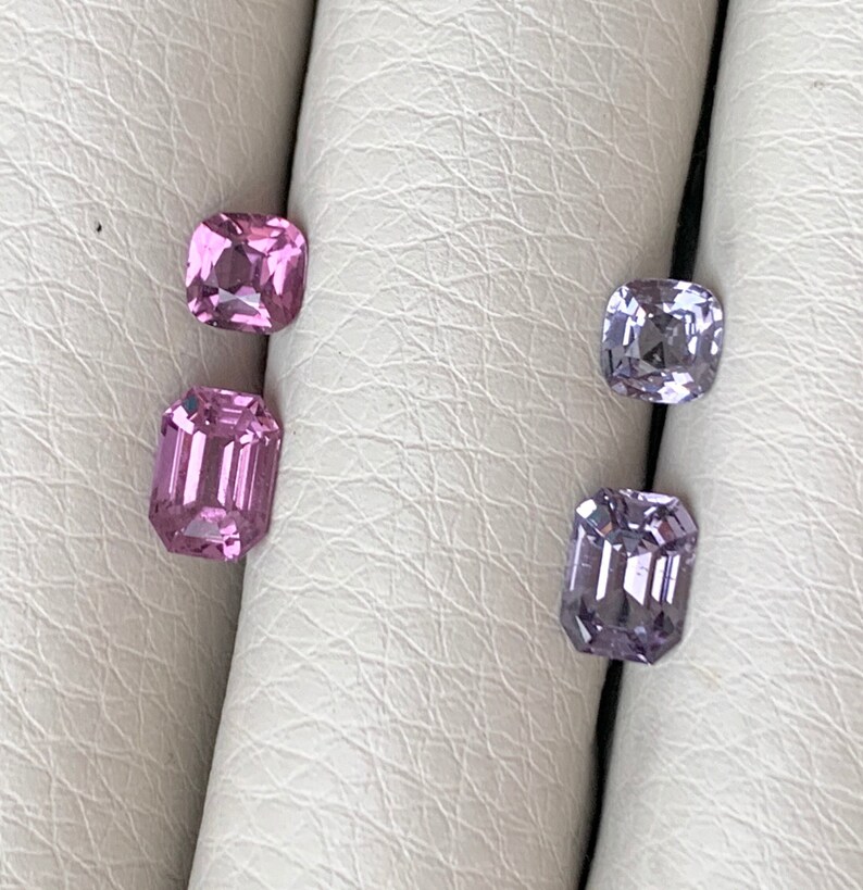 Pu&ograve; includere: Quattro pietre preziose sciolte, due rosa e due viola, sono esposte su una superficie bianca. Le pietre preziose sono tagliate in forma quadrata con bordi smussati.