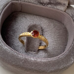 May include: A gold ring with a red gemstone and small diamonds set in the band.