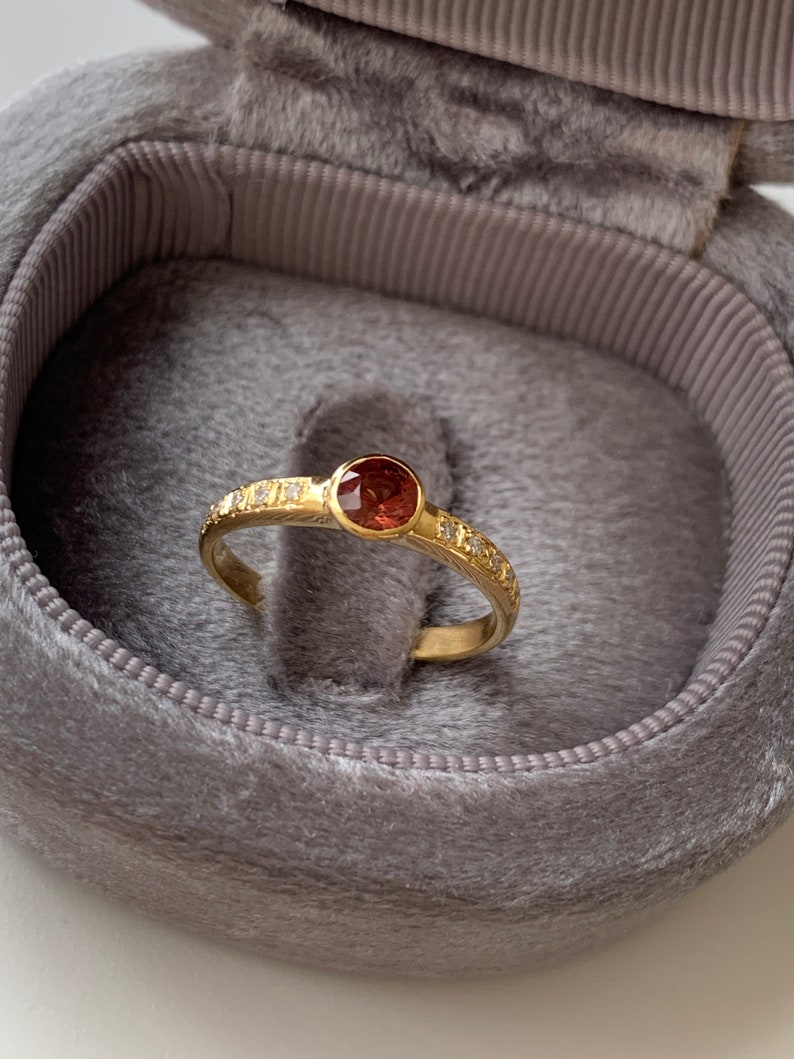 May include: A gold ring with a red gemstone and small diamonds set in the band.