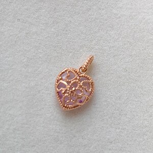 K&ouml;nnte beinhalten: Ein herzf&ouml;rmiger Anh&auml;nger aus Ros&eacute;gold mit einem filigranen Design. Der Anh&auml;nger ist mit einem kleinen, offenen Herzdesign verziert.
