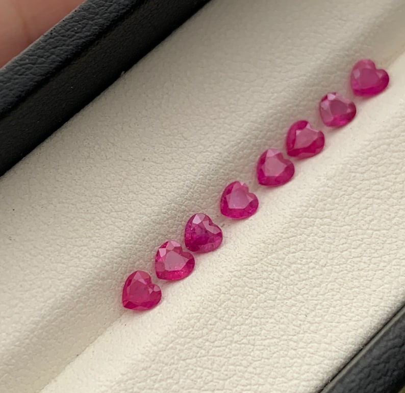 May include: A row of eight pink heart-shaped gemstones in a white velvet box.