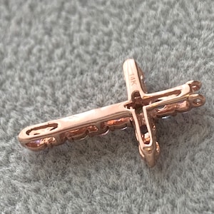 May include: A rose gold cross pendant with a 14K marking. The cross is detailed with small stones and has a loop for attaching to a chain.