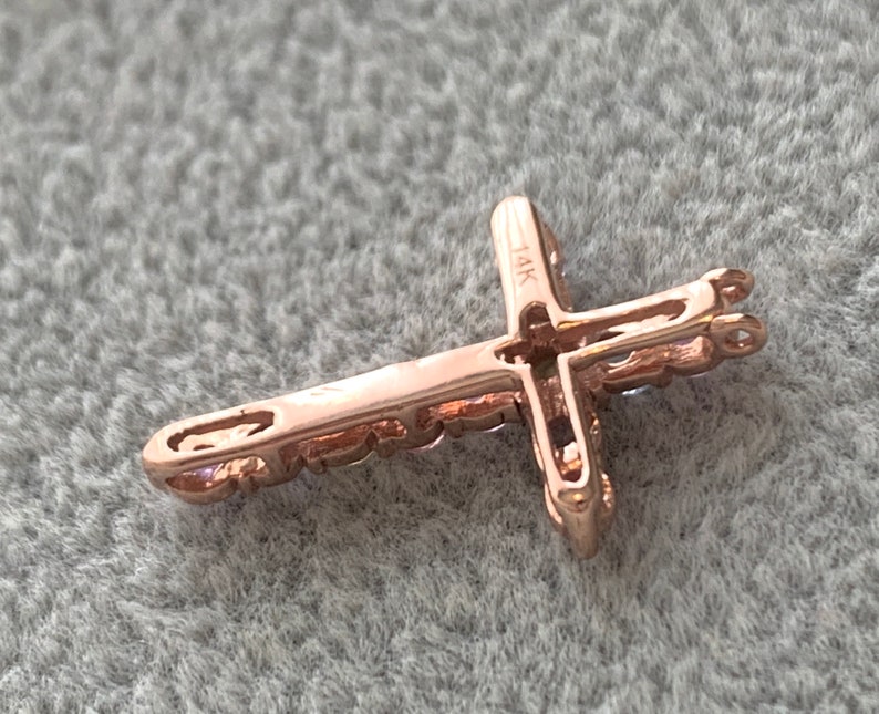 May include: A rose gold cross pendant with a 14K marking. The cross is detailed with small stones and has a loop for attaching to a chain.