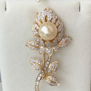 May include: A gold flower brooch with a large pearl in the centre and smaller diamonds surrounding the pearl and the flower petals.