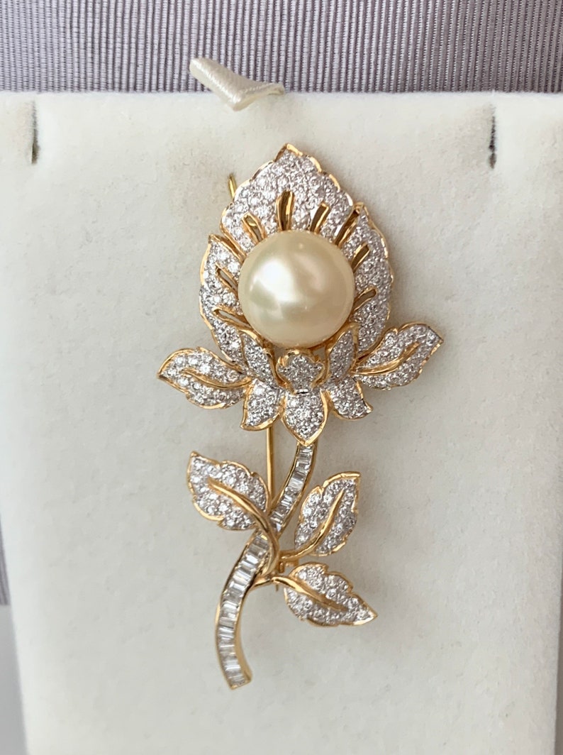 May include: A gold flower brooch with a large pearl in the centre and smaller diamonds surrounding the pearl and the flower petals.