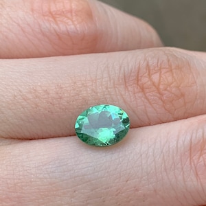 May include: A light green oval gemstone with a slight shimmer.