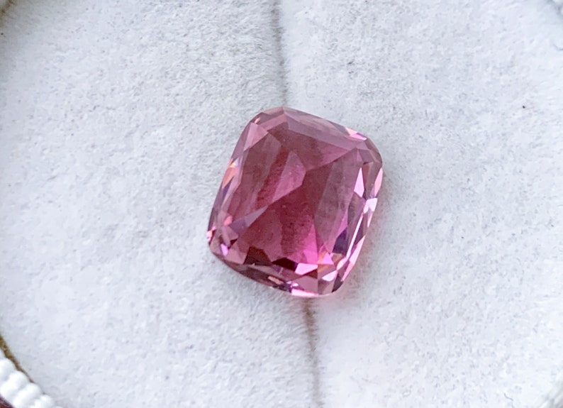 Puede incluir: Una piedra preciosa rosa con un corte de coj&iacute;n. La piedra est&aacute; facetada y tiene un acabado brillante.