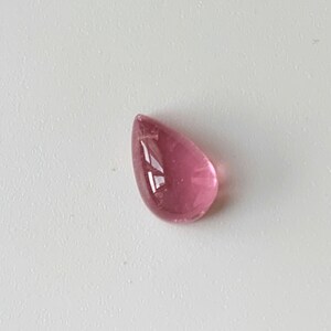 K&ouml;nnte beinhalten: Ein tropfenf&ouml;rmiger rosa Edelstein mit einer glatten, polierten Oberfl&auml;che.