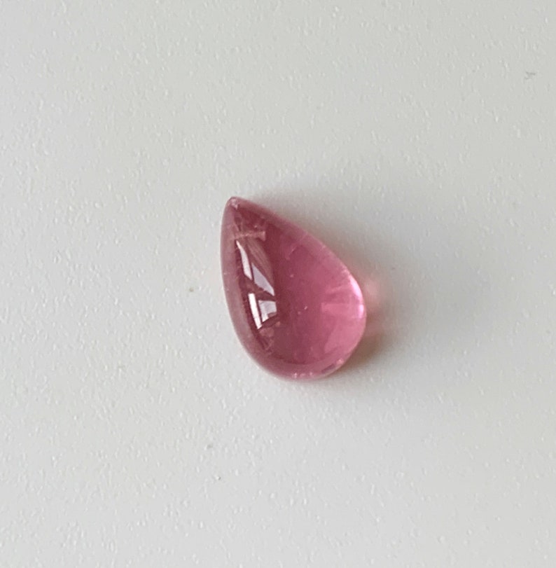 K&ouml;nnte beinhalten: Ein tropfenf&ouml;rmiger rosa Edelstein mit einer glatten, polierten Oberfl&auml;che.