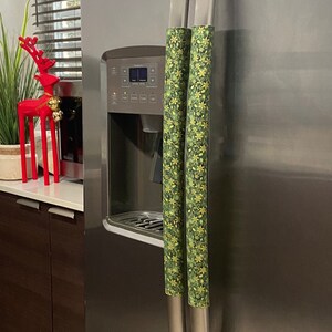 May include: Two green and gold floral patterned refrigerator handle covers on a stainless steel refrigerator.