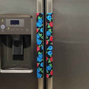 Puede incluir: Cubiertas para manijas de refrigerador con fondo negro y un estampado floral de rosas azules y rojas con hojas verdes. Las cubiertas están diseñadas para adaptarse a las manijas de un refrigerador.