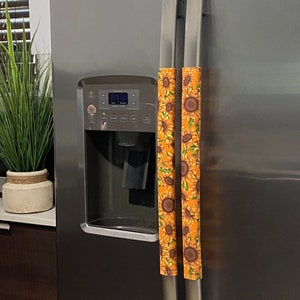 Pode incluir: Duas capas para puxadores de geladeira com estampa de girassol em laranja e amarelo. As capas são de tecido e são presas aos puxadores com velcro.