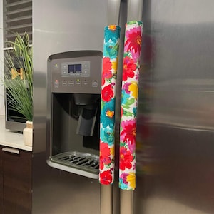 Puede incluir: Dos cubiertas para manijas de refrigerador con estampado floral colorido. Las cubiertas son de tela y tienen un fondo blanco con flores rojas, rosas, amarillas y azules.