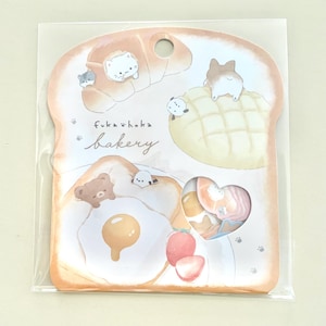 May include: A novelty notepad in the shape of a slice of bread, with illustrations of baked goods and adorable animal characters. The notepad features the text "Fuka hoka bakery". The design incorporates a variety of colors and is die-cut.