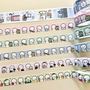Puede incluir: Varios rollos de cinta adhesiva washi con patrones repetidos de pequeñas figuras de dibujos animados. Los diseños incluyen figuras con libros, comida y otros objetos. Algunas cintas tienen un diseño de sello con ilustraciones.