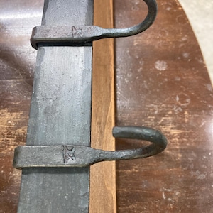 May include: Two black metal hooks mounted on a wooden surface. The hooks are curved and have a simple design.