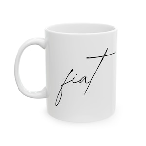 May include: White ceramic mug with a curved handle. The mug displays the word "fiat" in black, handwritten script. The mug is a standard size and shape, suitable for tea or coffee.
