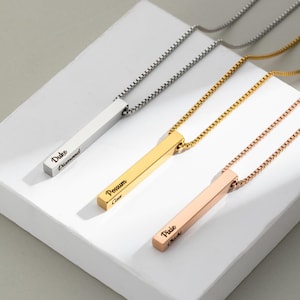 Puede incluir: Tres collares de barra personalizados en plata, oro y oro rosa. Cada collar presenta un colgante rectangular con texto grabado. El collar plateado dice "Duke Diamond", el dorado "Possum Cass" y el oro rosa "Pixie Chichi".