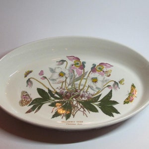 Peut inclure: Plat à four ovale en céramique blanche avec un motif floral composé de fleurs roses et blanches, de feuilles vertes et de papillons dorés. Le texte "HELLEBORUS NIGER Christmas Rose" est imprimé au fond du plat.