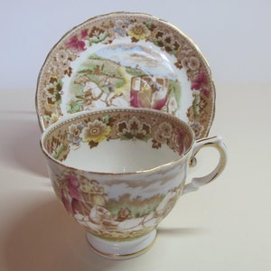Peut inclure: Une tasse à thé et une soucoupe vintage avec un motif floral et une scène de calèche. La tasse et la soucoupe sont blanches avec des bordures dorées.